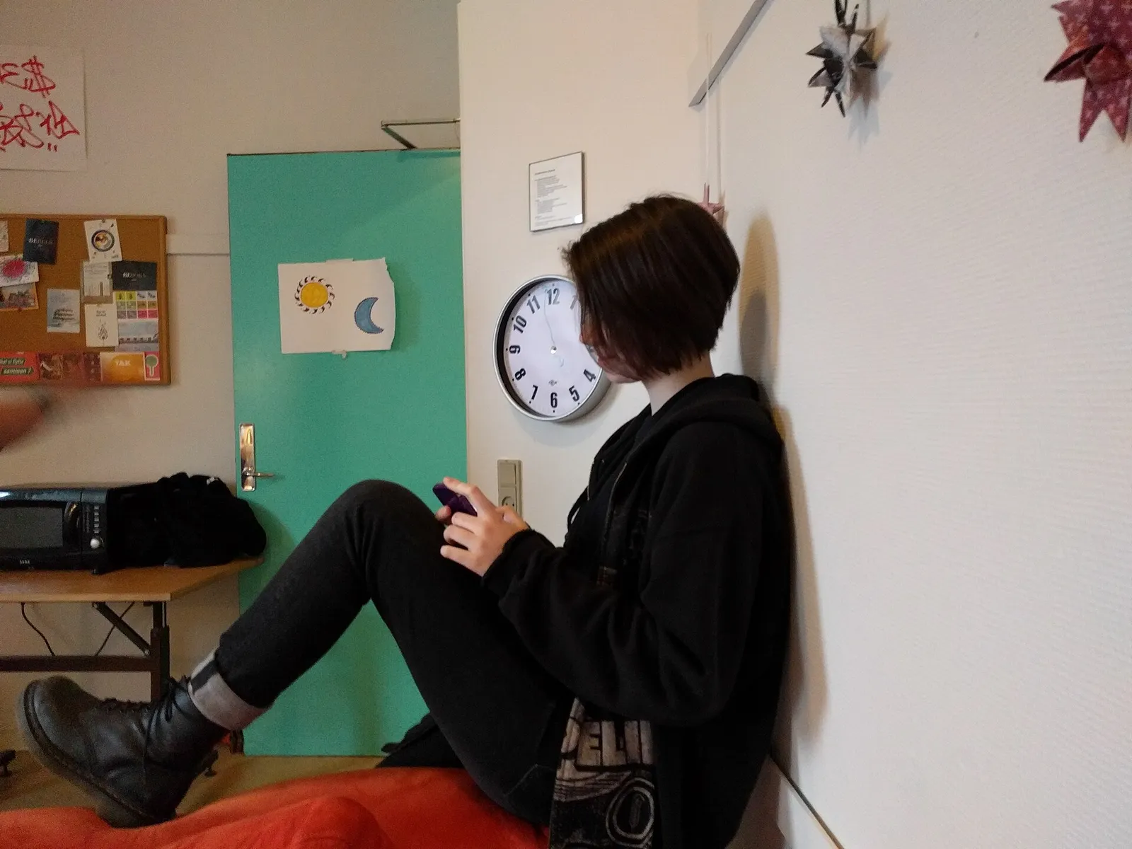 Jugendliche Person sitzt allein in einem Zimmer und blickt auf ihr Smartphone